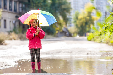 Adorable little girl holding white umbrella standing in a puddle on warm autumn day