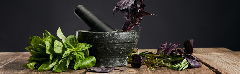 panoramic shot of mortar and pestle with basil on wooden table isolated on black
