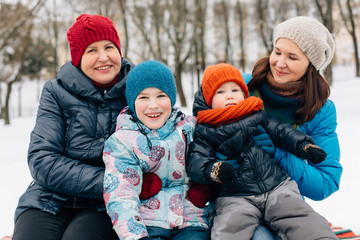 Fototapeta na wymiar Happy family having fun in winter park. Grandmother with daughter and grandchildren playing outdoors on blanket.