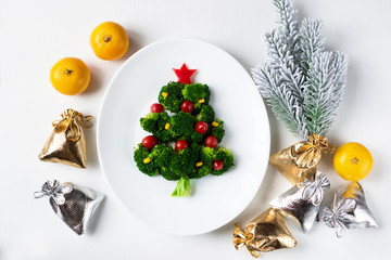 Christmas edible tree made from broccoli, tomato and corn on a white plate. Christmas card with...