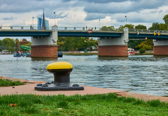 Fototapeta premium Yellow bollard for the line for mooring riverboats, with river and bridge blurred in the background (selective focus on the bollard)