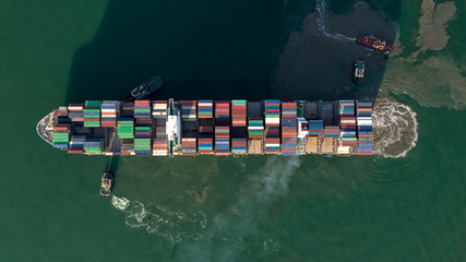 Aerial top view Tugboat pushing container ship to quayside for load/unload container via crane for logistics, import export, shipping or transportation.