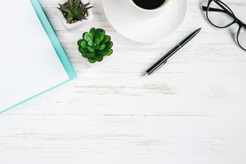 Notebook, pen, glasses, plants succulents, a cup of coffee on a white wooden table, flat lay, top view. Office table desk, workplace