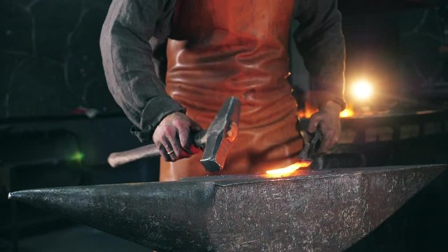 Blacksmith is using hammer to forge metal