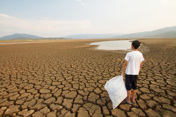 Young man holding full plactic bags while looking to the drying lake metaphor Drought and Plastic...