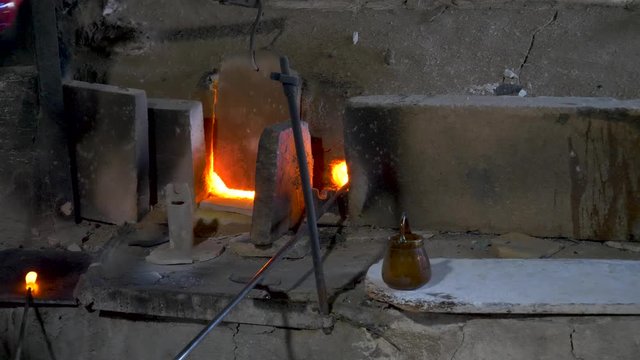 Heating molten glass in a furnace, the glassblower then forms a handle on a glass vase