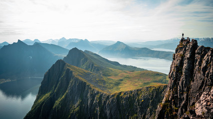 Adventurous man is standing on top of the mountain and enjoying the beautiful view during a vibrant sunset. Taken on top Senja, Norway 