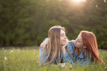 Two girls lie on the grass and look at each other.