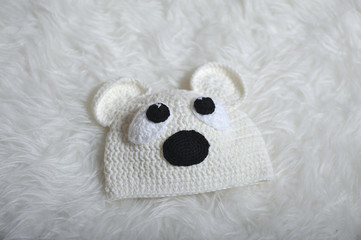 Cute children's knitted hat in the form of a teddy bear on a white carpet background, close-up. Cap for newborns