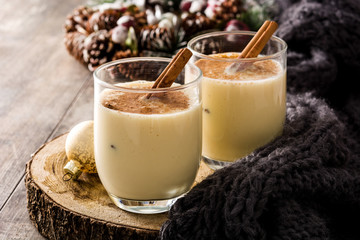Homemade eggnog with cinnamon in glass on wooden table. Typical Christmas dessert. 
