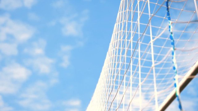 Soccer ball in goal net against blue sky.