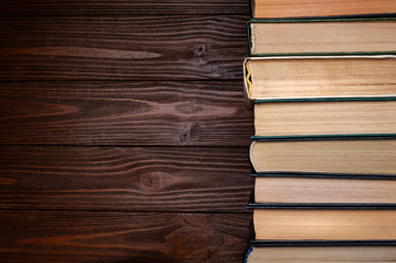 Old books . A number of old used closed books with hardcover in dust on dark wooden background with space for text.