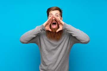 Redhead man with long beard over isolated blue background shouting and announcing something