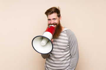 Redhead man with long beard over isolated background shouting through a megaphone