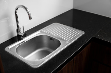 Close up on modern kitchen metal faucet and metal kitchen sink.