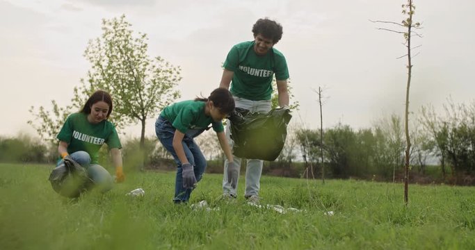 Volunteers in park picking up trash. Ecological movement activists collecting garbage and sorting it out. Friends of different age taking care of nature - 4k