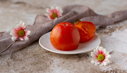 Ripe juicy persimmons on white plate, autumn fruit and flowers