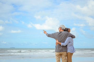 Fototapeta na wymiar A senior couple hugged each other at the beach in the morning. The old man pointed the finger to the old woman to look at the bright blue sky, life insurance plan at the retirement concept.