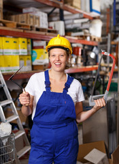 Woman  in uniform and helmet standing near racks in build store holding saw