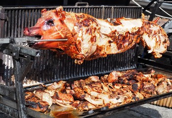 Whole large pig on rotary spit grill, with the slices of meat cut flat during cooking  
