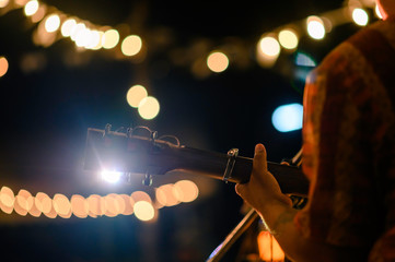 Rear view of the man sitting play acoustic guitar on the outdoor concert with a microphone stand in...