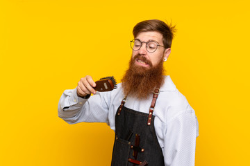 Barber with long beard in an apron over isolated yellow background