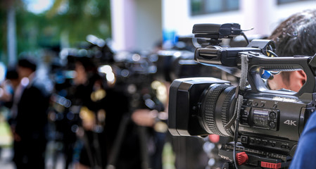 Press conference.Close-up of Video camera on blurred group of press and media photographer as...