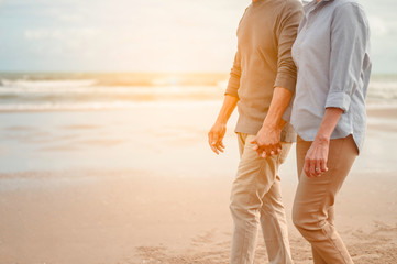 Senior lovers walk hand in hand at the beach at sunset, plan life insurance at retirement concept.