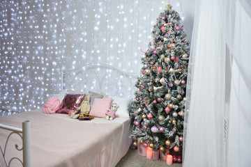 Beautiful interior against the background of a white wall with cold garlands, a forged bed and a Christmas tree. Garland on the whole wall, place for text