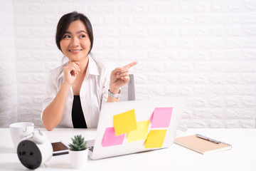 Happy woman sitting at home office and pointing to copy space