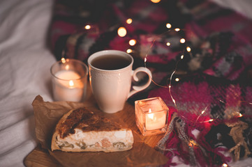 Cup of black tea with tasty pie, burning candles and glowing lights close up. Evening time.