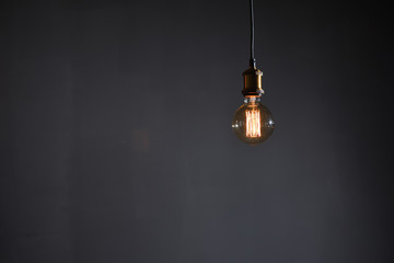 Beautiful large round retro lamp with incandescent threads glows on a background of a gray wall, closeup.