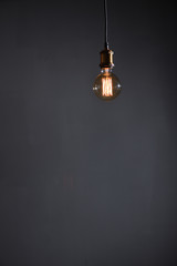 Beautiful large round retro lamp with incandescent threads glows on a background of a gray wall,...