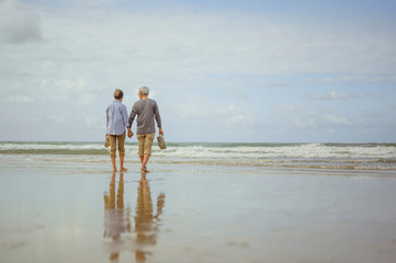Senior couple walking on the beach holding hands at sunrise, plan life insurance at retirement concept.