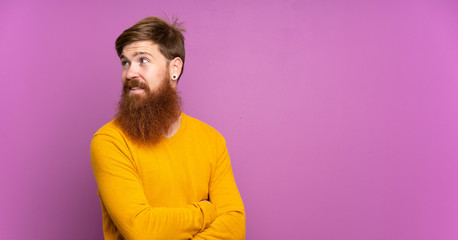 Redhead man with long beard over isolated purple background with arms crossed and happy