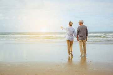 Senior couple standing on the beach holding hands at sunrise, plan life insurance at retirement concept.