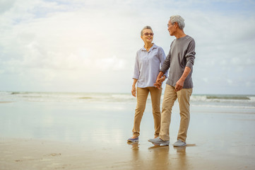 Senior couple walking on the beach holding hands at sunrise, plan life insurance at retirement concept.