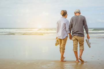 Senior couple walking on the beach holding hands at sunrise, plan life insurance at retirement...