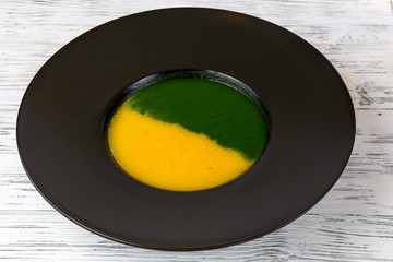 Spinach and pumpkin soup in a black plate.