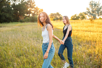 Naklejka na ściany i meble Two attractive young women are walking outdoors under sunlight. Best friends