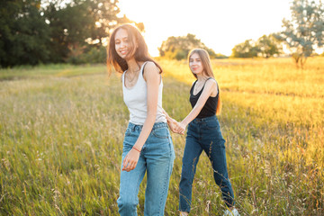 Naklejka na ściany i meble Two attractive young women walking outdoors under sunlight. Best friends