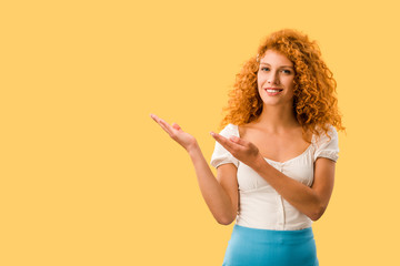 happy woman with red hair presenting something isolated on yellow
