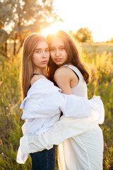 Fototapeta premium Two young women standing together and hugging on the field under sunlight