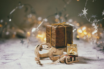 Christmas wood toys sled with gift boxes and lightning garlands over old white wooden table. Christmas and New year decorations or greeting card.