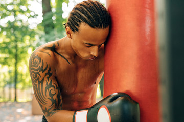 Tired boxer leaning against a punching bag wearing boxing gloves looking down