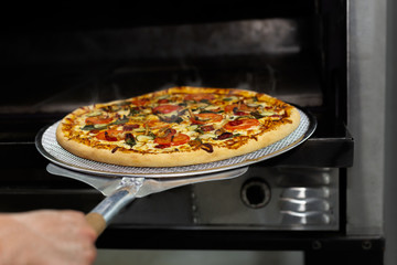 Chef putting pizza baking sheet in oven at restaurant with pizza shovel.
