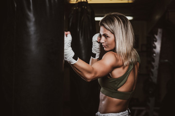 Muscular pretty woman is doing her kickboxing exercises with punching bag.