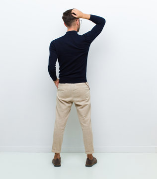 Young Full Body Man Feeling Clueless And Confused, Thinking A Solution, With Hand On Hip And Other On Head, Rear View Against White Background