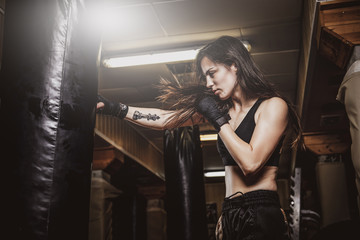 Fototapeta na wymiar Skinny focused woman has a boxing training with punching bag at dark gym.