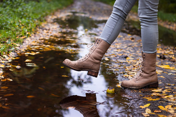 Waterproof leather boots over puddle with reflection. Hiking boot at autumn season